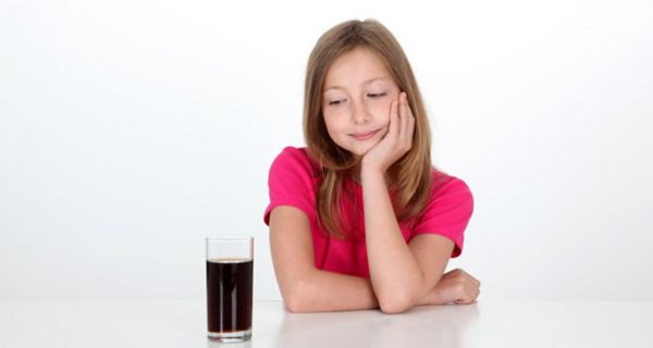 Mädchen mit langen, braunen Haaren, ca. 10/11 Jahre alt, in Kurzarmpoloshirt, Kopf in linke Hand gestützt, schaut sehnsüchtig auf ein Glas Cola