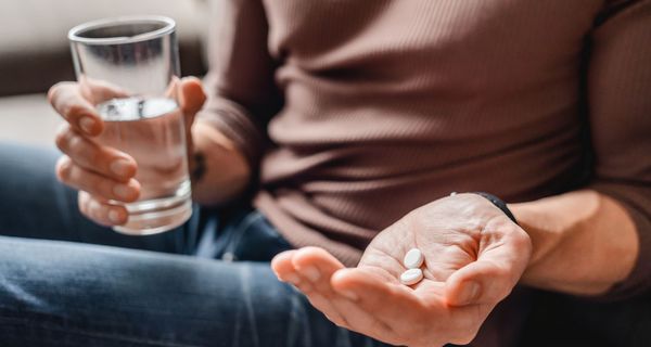 Mann, hält ein Glas mit Wasser und zwei Tabletten in den Händen.