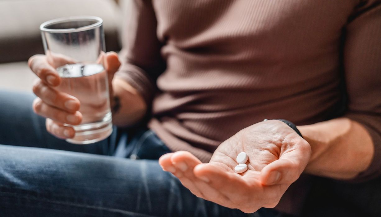 Mann, hält ein Glas mit Wasser und zwei Tabletten in den Händen.