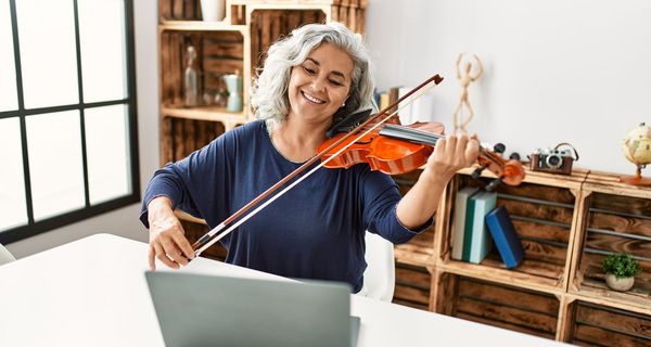 Ältere Frau mit Geige vor dem Laptop.