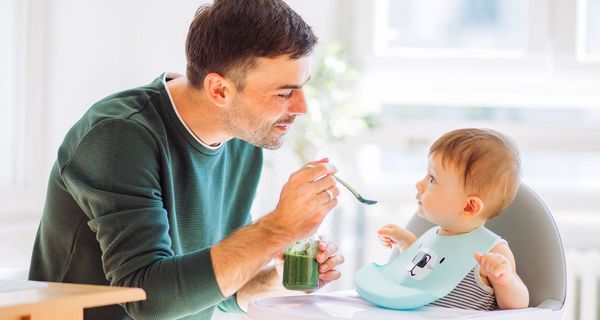 Vater füttert sein kleines Kind mit einem Löffel.
