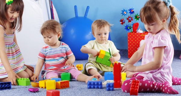 Vier Kindergartenkinder unterschiedlichen Alters beim Spielen mit buntem Spielzeug