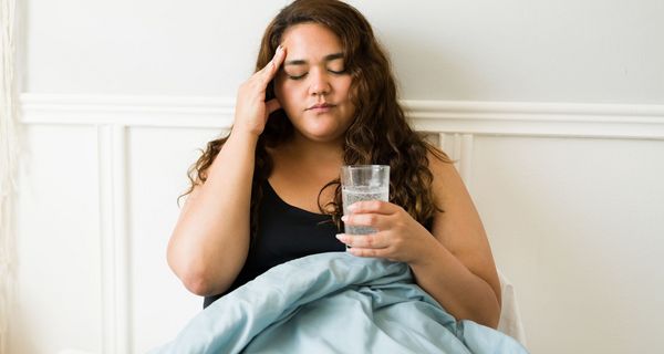 Junge Frau, sitzt mit Kopfschmerzen im Bett.