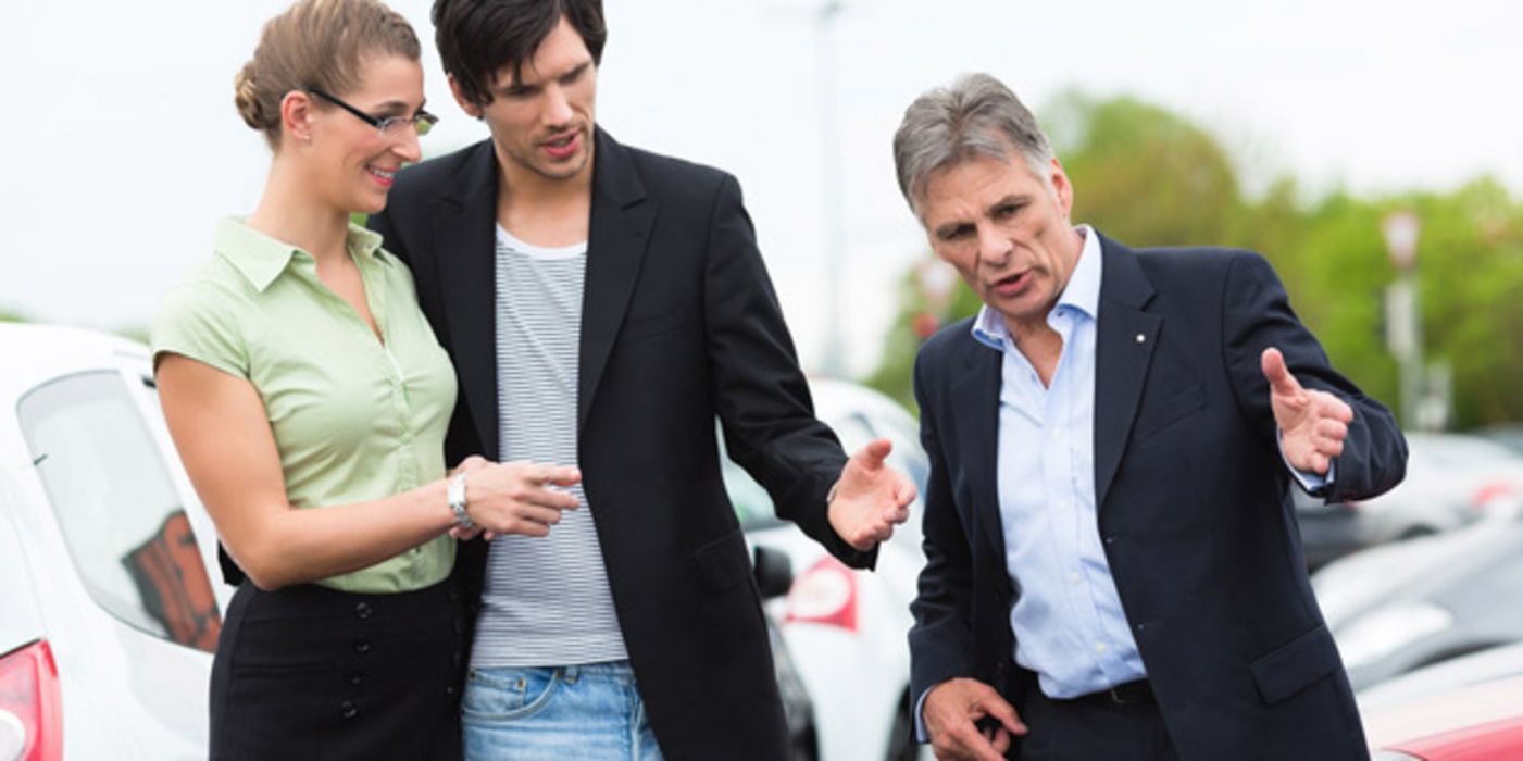 Junges Paar mit Autohändler beim Verhandeln