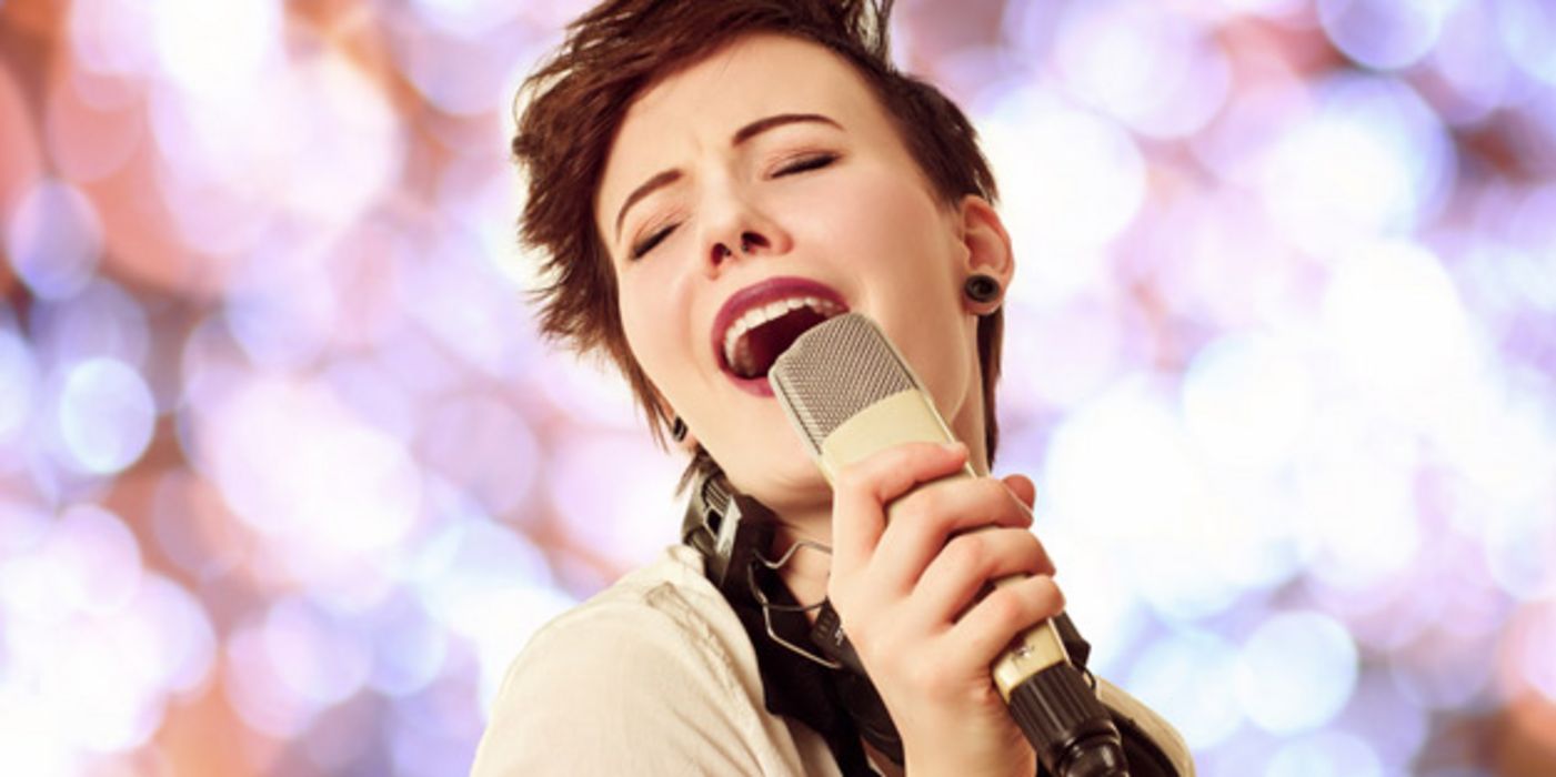 Junge dunkelhaarige Frau singt hingebungsvoll mit zurückgelegtem Kopf und geschlossenen Augen, ein Mikrofon in der Hand