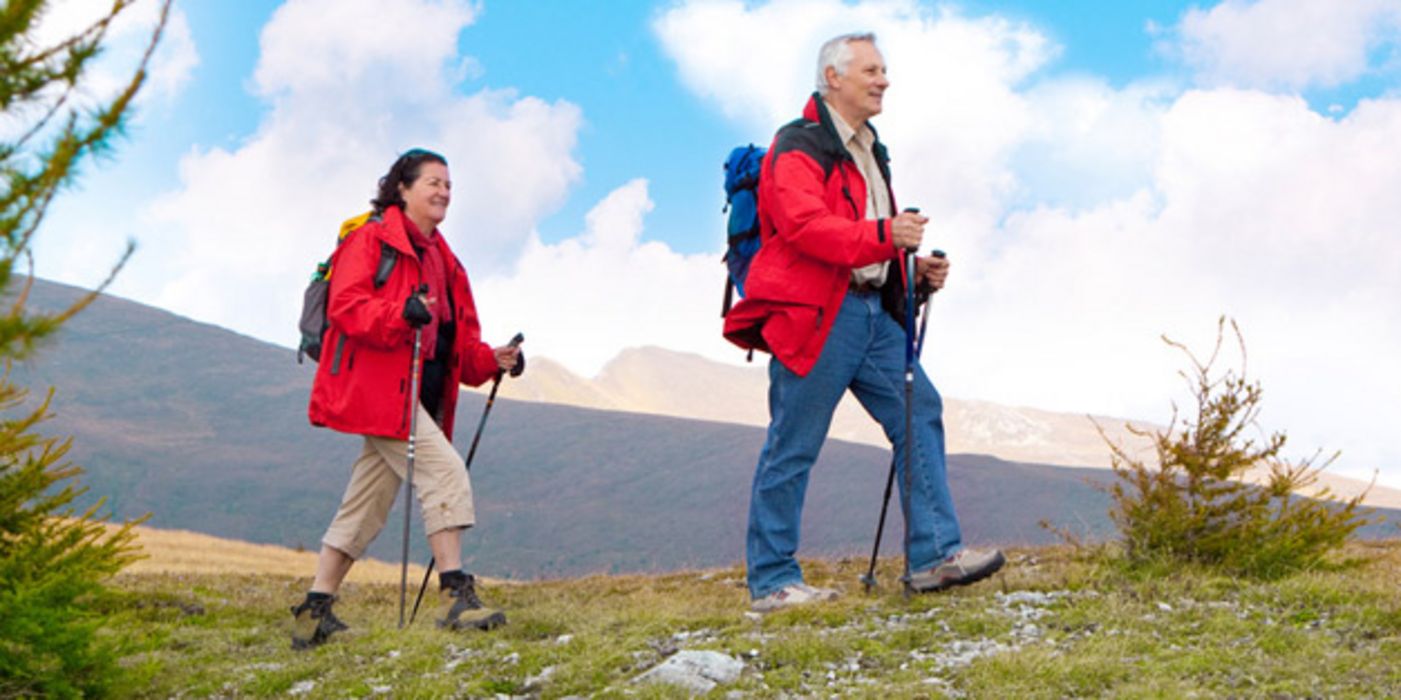 Älteres Paar in den 60ern, beide knallrote Wanderanoraks, mit Wanderstöcken beim Wandern in den Bergen