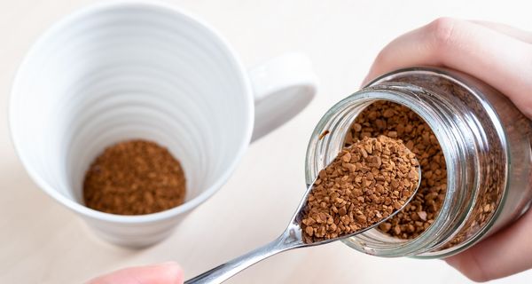 Jemand löffelt Instant-Kaffee-Pulver in eine Tasse. Nur die Hände sind zu sehen.