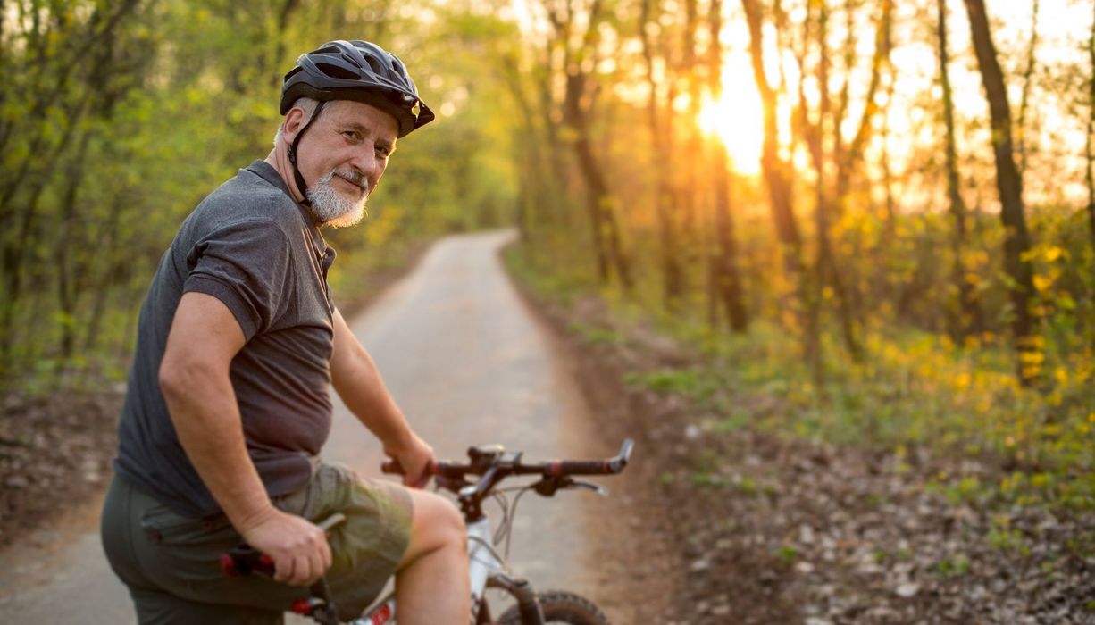 Älterer Herr mit leichtem Bauchansatz, Fahrrad und Helm auf einem Waldweg.