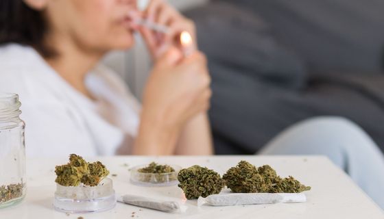 Im Vordergrund: Cannabis in Gläsern und auf einem offenen Joint-Papier.