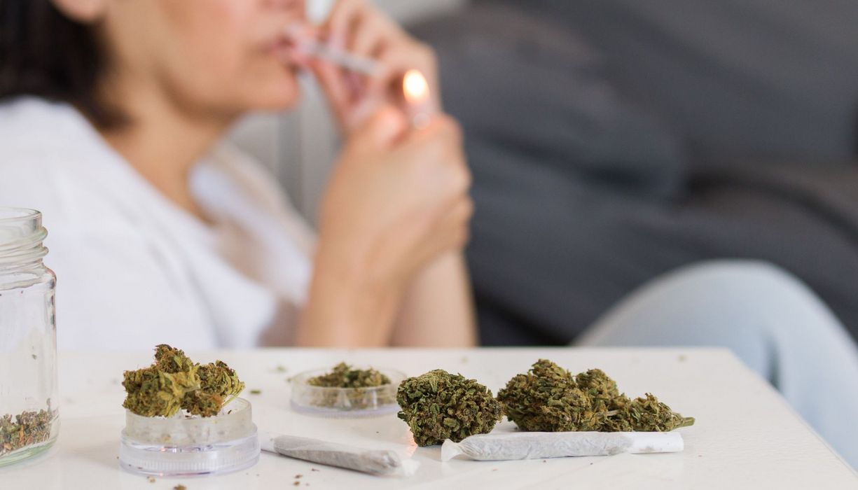 Im Vordergrund: Cannabis in Gläsern und auf einem offenen Joint-Papier.