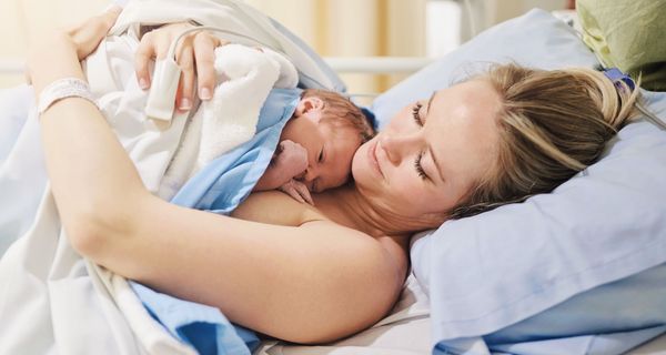 Baby liegt im Krankenhaus auf der Brust der Mutter, beide nackt und zugedeckt.
