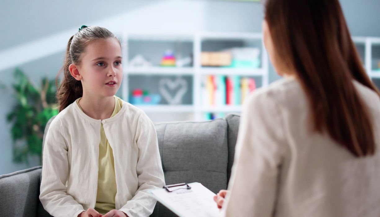 Mädchen, etwa 10 Jahre alt, sitzt einer Erwachsenen mit Klemmbrett gegenüber.