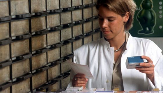 Apothekerin hält ein Rezept in der Hand und sucht ein Arzneimittel aus einer Schublade