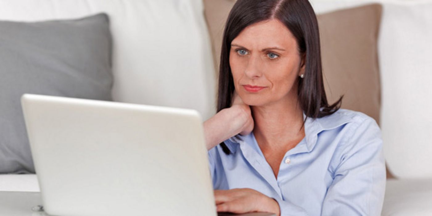 Frau sitzt an einem Laptop und betrachtet skeptisch den Bildschirm