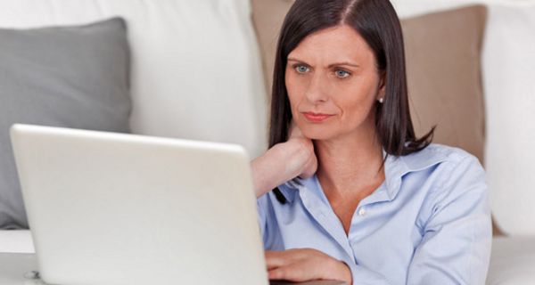 Frau sitzt an einem Laptop und betrachtet skeptisch den Bildschirm