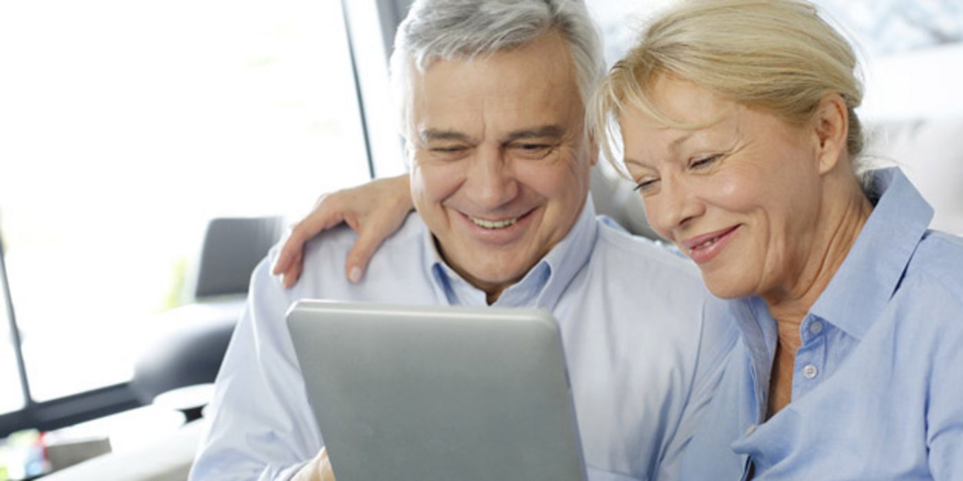 Älteres Paar bedient einen Tablet-Computer und lacht dabei