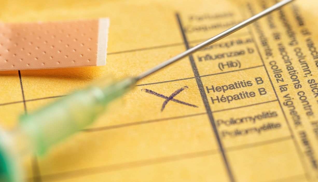 Spritze mit gelbem Impfbuch und einem Kreuz bei Hepatitis B. 