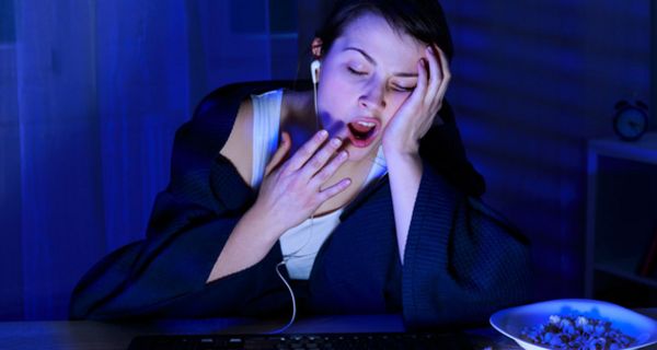 Junge Frau am Computer geht spät zu Bett und gähnt.