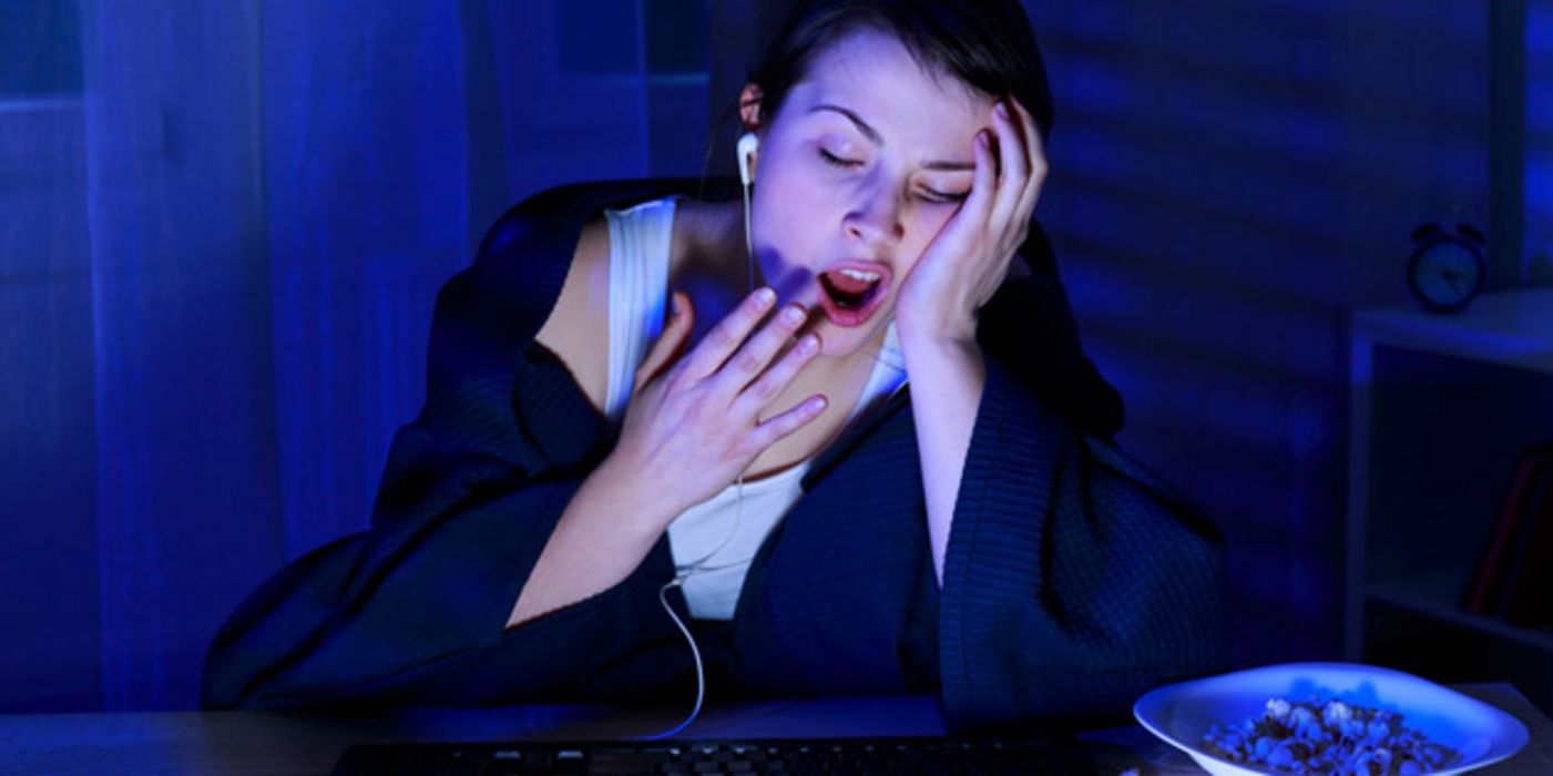 Junge Frau am Computer geht spät zu Bett und gähnt.