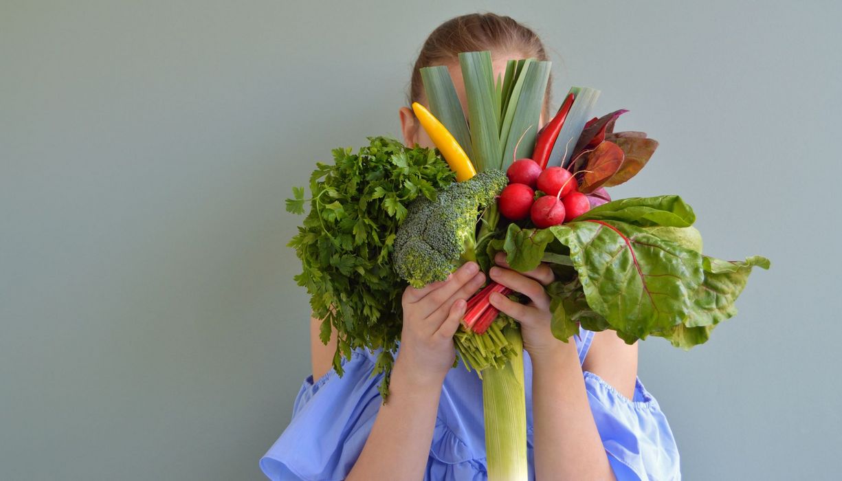 Frau, hält sich Gemüse vor das Gesicht.