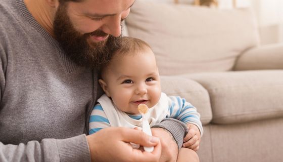 Vater füttert Baby mit Brei.