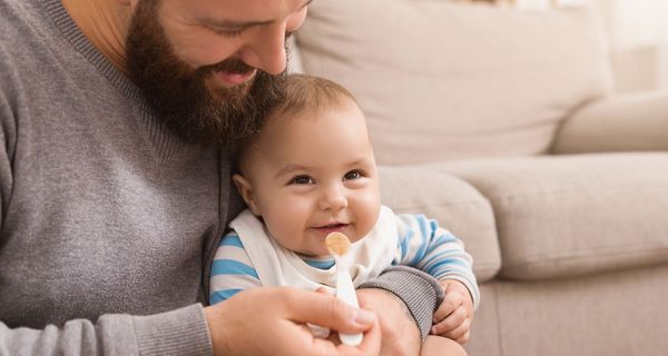 Vater füttert Baby mit Brei.