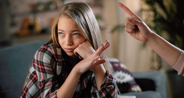 Junges Mädchen schaut genervt zur Seite, während ihre Mutter sie mit dem erhobenen Finger streng zurecht weist. 