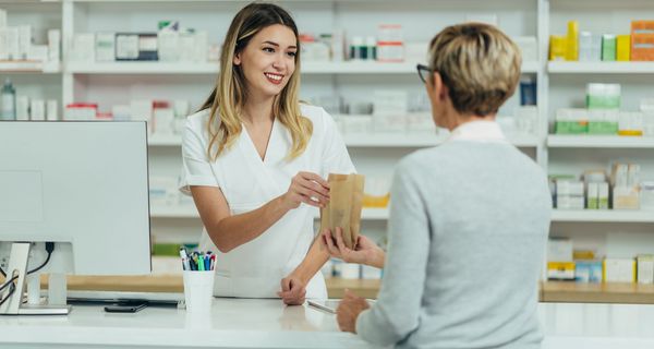 Apothekerin, reicht einer Kundin Medikamente.