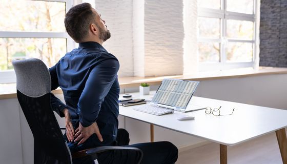 Mann am Schreibtisch hält sich den Rücken.