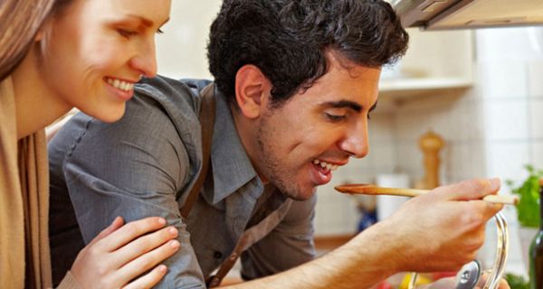 Mann und Frau beim Kochen. Er kostet von einem Kochlöffel mit Essen.