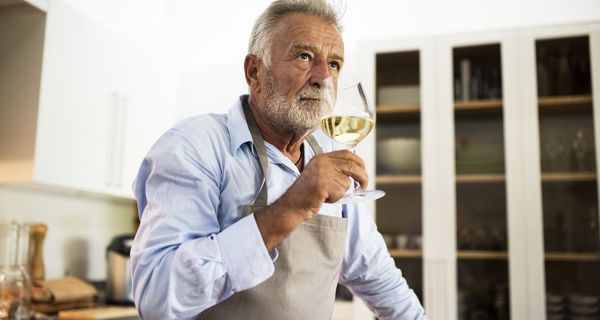 Grauhaariger Mann trinkt ein Glas Weißwein.