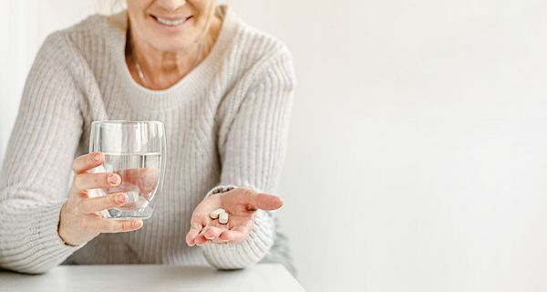 Ältere Frau, hält ein Glas Wasser und zwei Tabletten in der Hand.