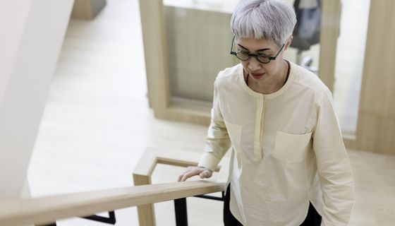 Eine Dame mit Brille und grauen Haaren steigt eine Treppe hoch.