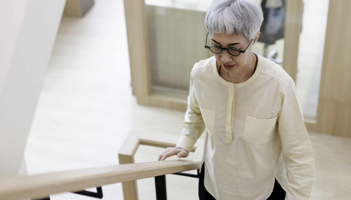 Eine Dame mit Brille und grauen Haaren steigt eine Treppe hoch.