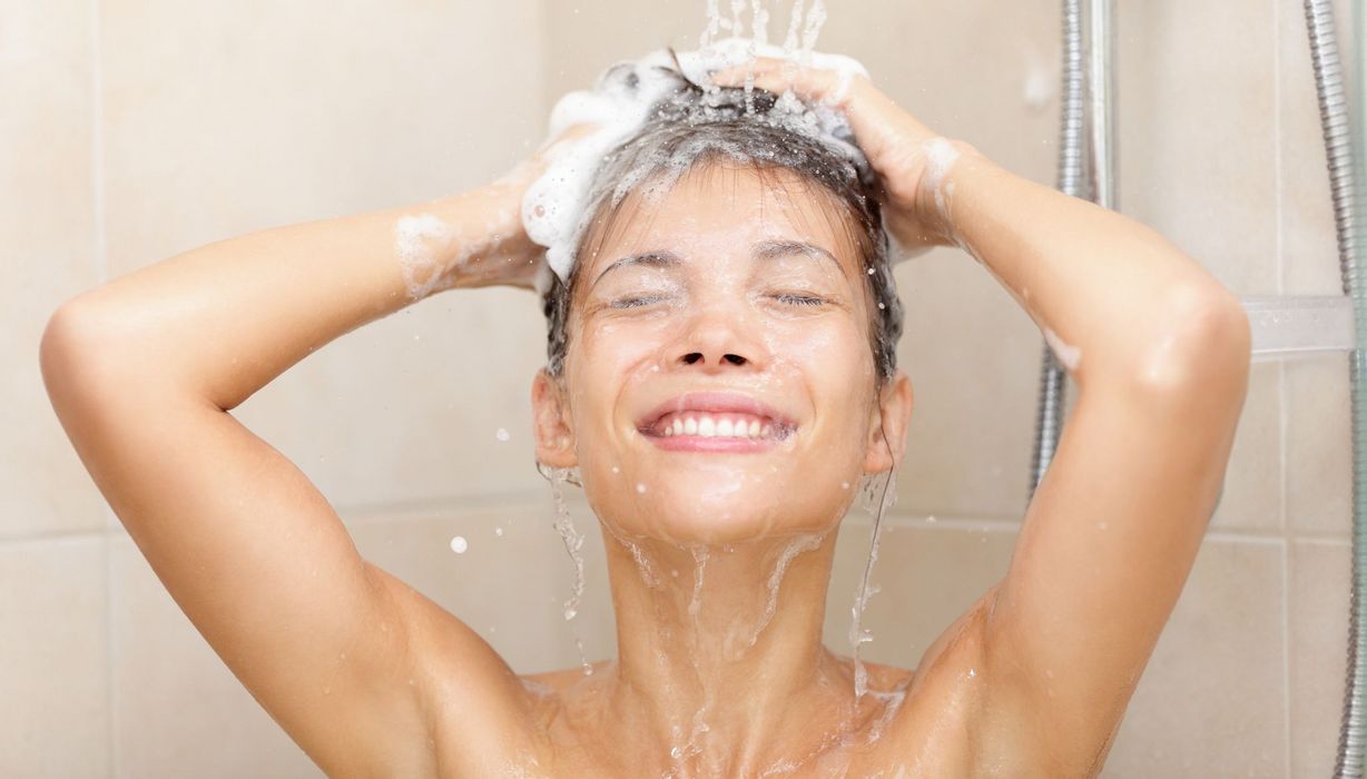 Junge Frau mit kurzen Haaren unter der Dusche, sie ist nur bis zum Schlüsselbein zu sehen.