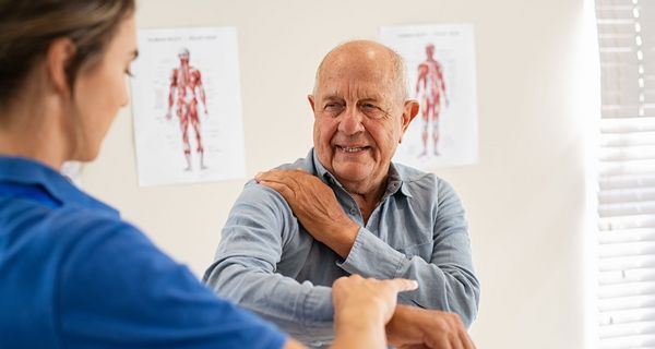 Mann mit schmerzender Schulter bei einer Ärztin.