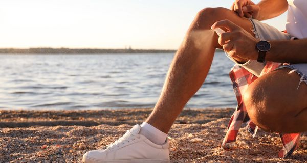 Mann ist am Strand und sprüht sich ein.