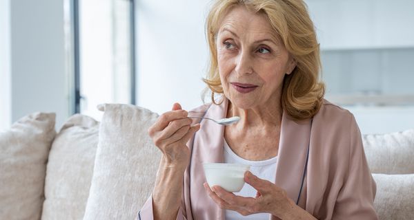Ältere Frau, isst einen Becher Joghurt.