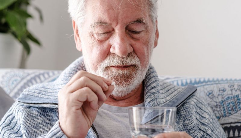 Ein älterer Herr nimmt eine Tablette mit einem Glas Wasser ein.