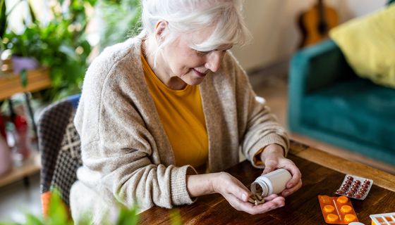 Eine ältere Frau, weißes Haar, schüttet sich Tabletten auf eine Hand.