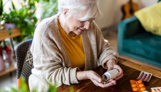 Eine ältere Frau, weißes Haar, schüttet sich Tabletten auf eine Hand.