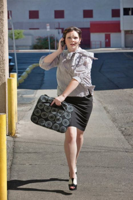 Mittelalte Frau, die mit Aktentasche in der Hand eine Straße entlang rennt, und mit dem Handy telefoniert