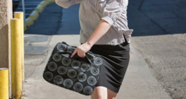Mittelalte Frau, die mit Aktentasche in der Hand eine Straße entlang rennt, und mit dem Handy telefoniert