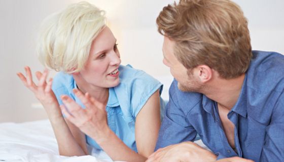 Junges Paar, bäuchlings in Freizeitkleidung auf einem Bett liegend, diskutiert miteinander