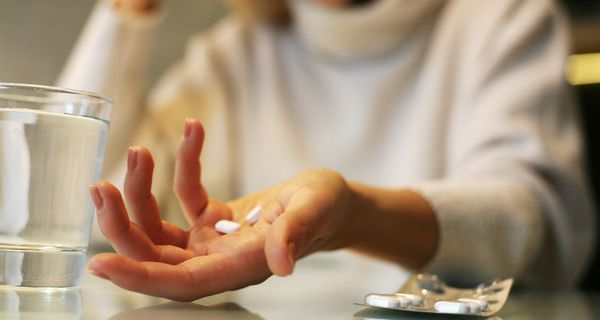 Frau, hält mehrere Tabletten in einer Hand, daneben ein Glas Wasser.