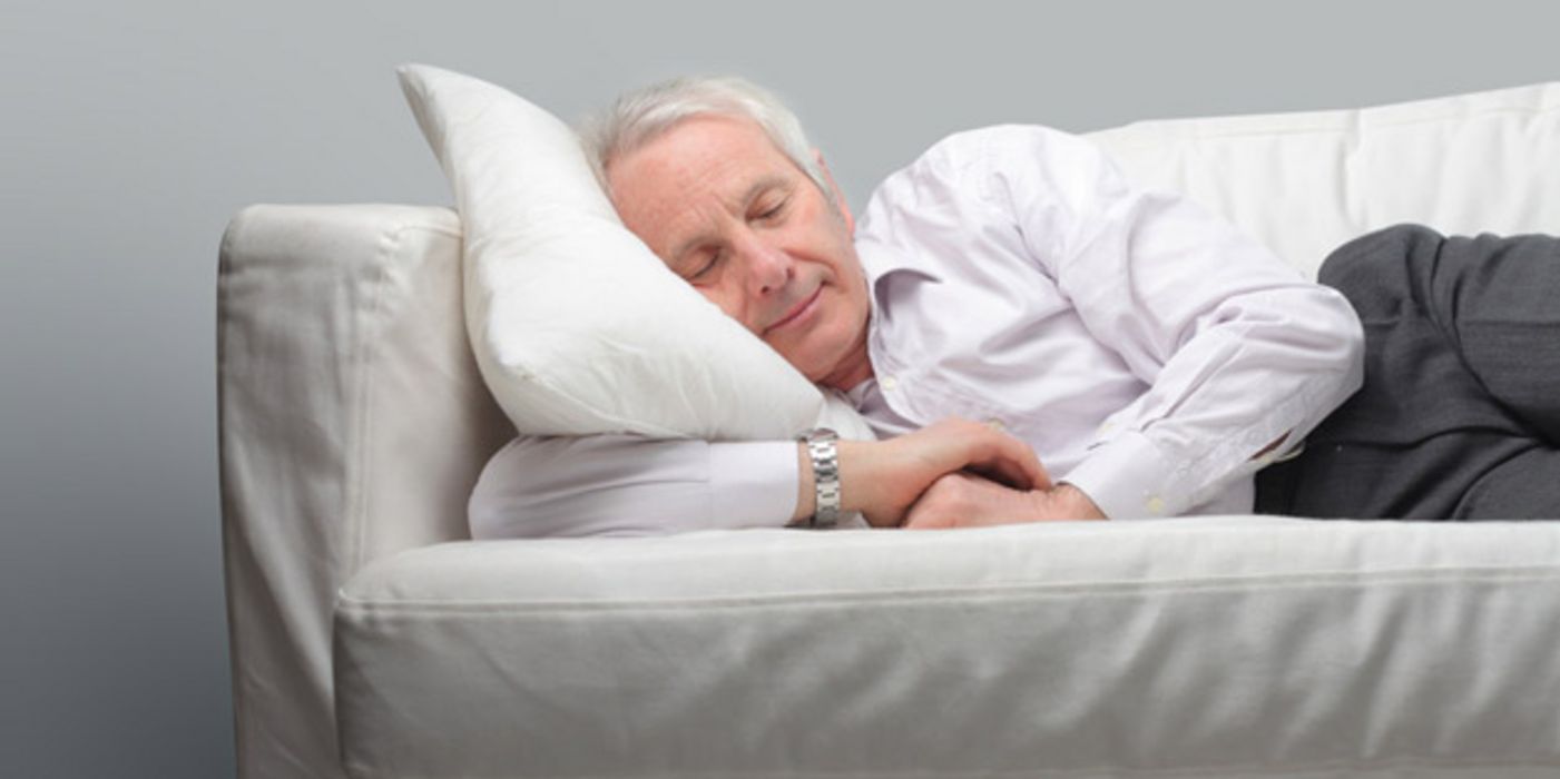 Weißhaariger Mann schläft auf dem Sofa.