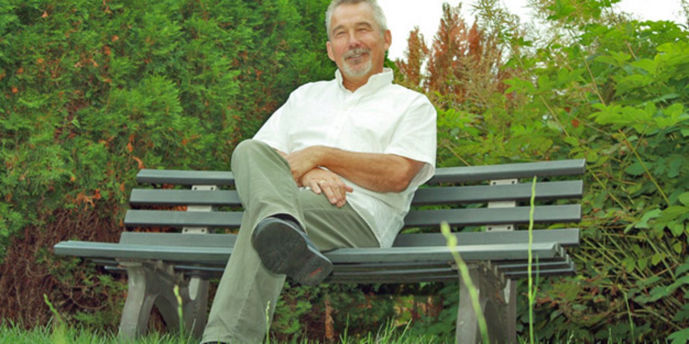 Älterer Mann sitzt auf einer Bank im Grünen