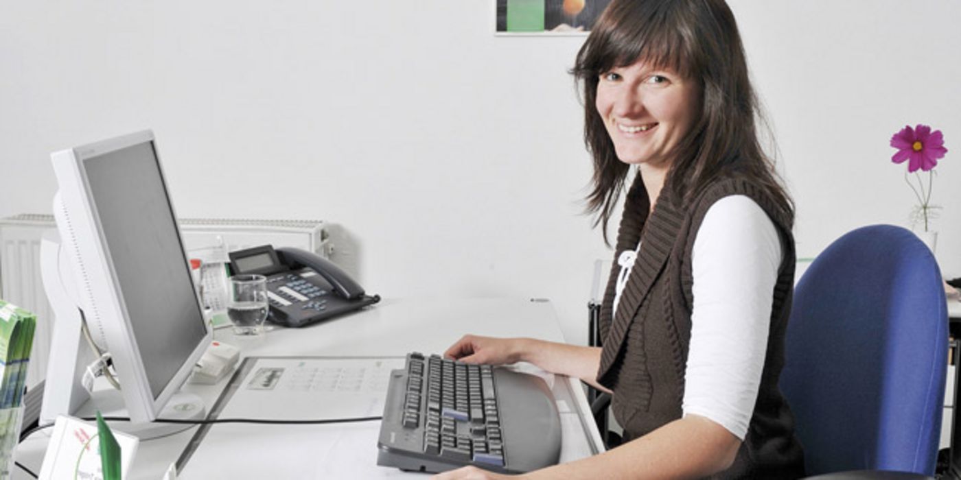Frau am Büro-Schreibtisch mit Tastatur und Bildschirm.