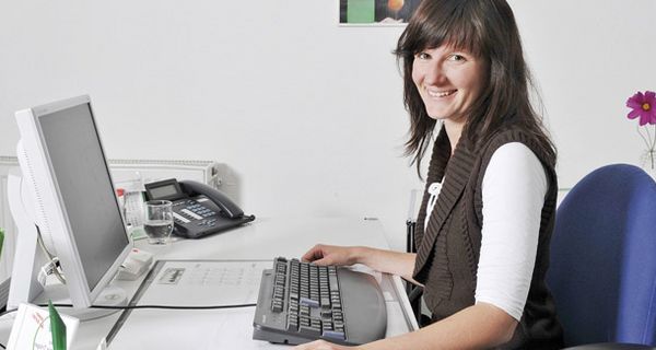 Frau am Büro-Schreibtisch mit Tastatur und Bildschirm.