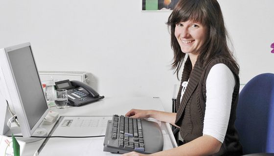 Frau am Büro-Schreibtisch mit Tastatur und Bildschirm.